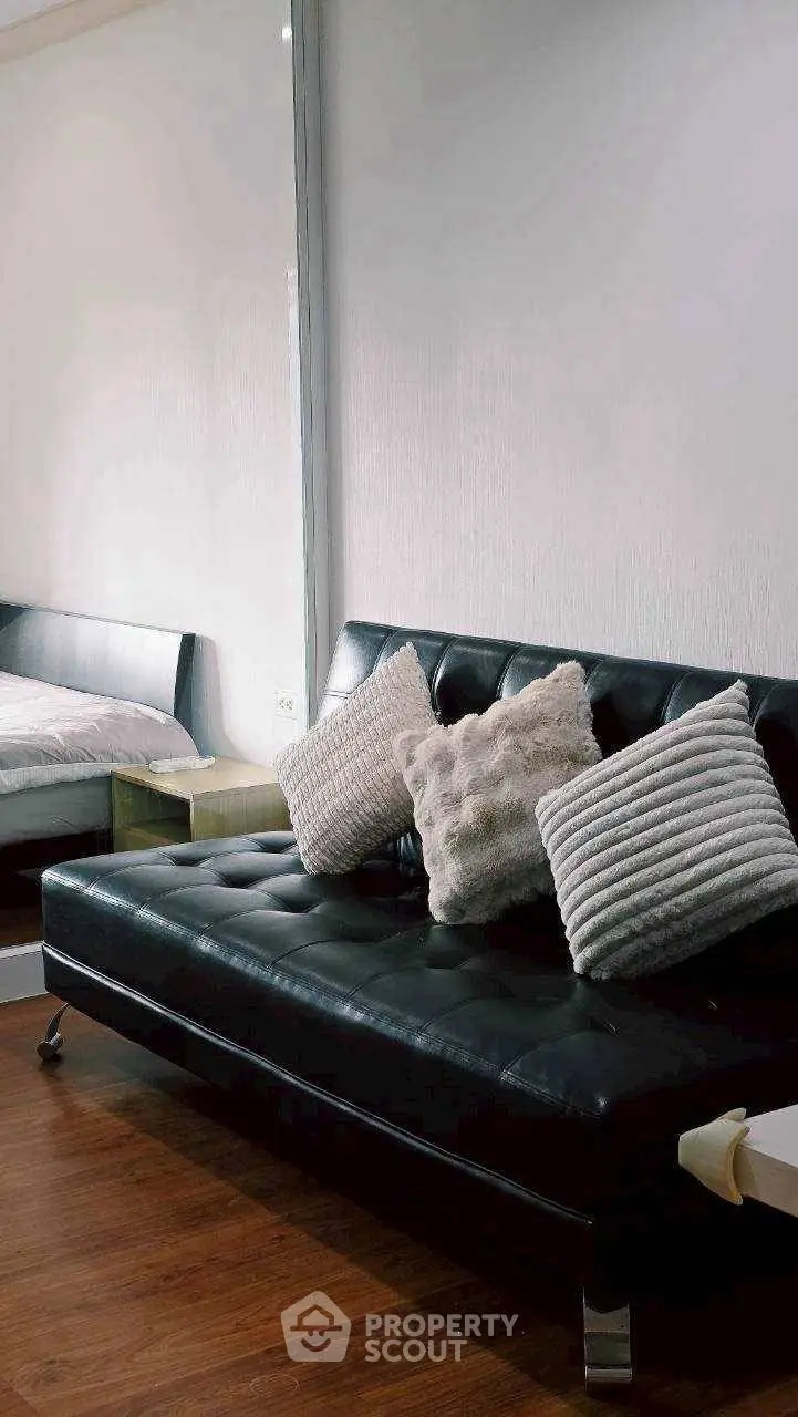 Modern living room with sleek black leather sofa and cozy cushions, adjacent to a stylish bedroom.