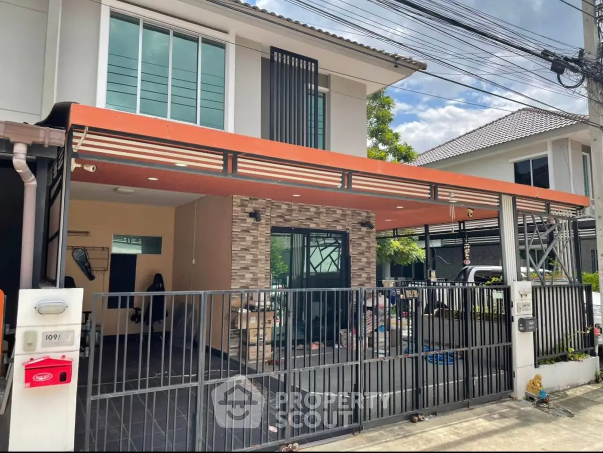Modern two-story house with gated entrance and carport in suburban neighborhood.