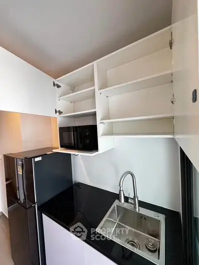 Modern kitchen with sleek black countertop, stainless steel sink, and open shelving for storage.