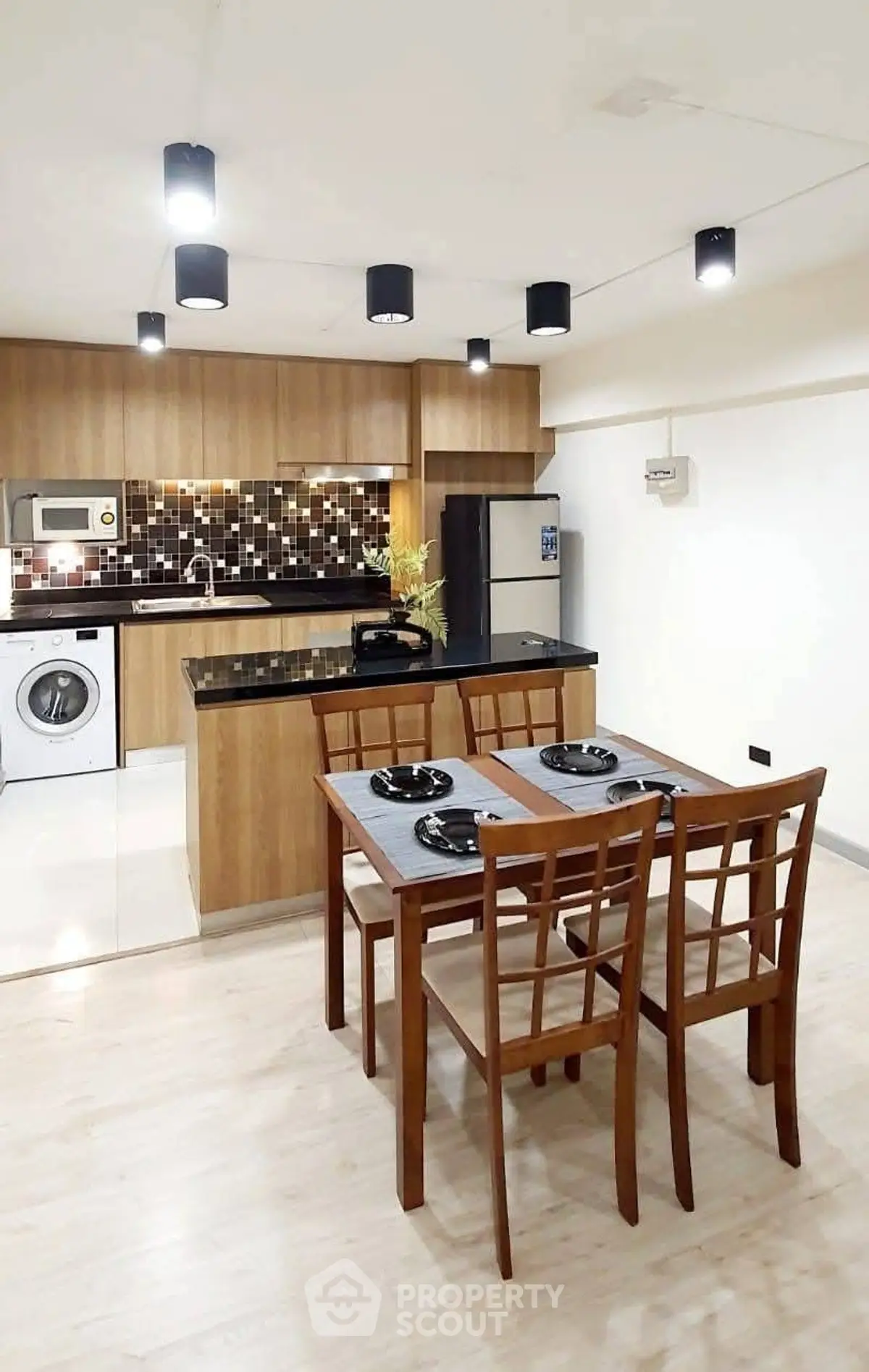 Modern kitchen with dining area, featuring wooden cabinets, washing machine, and stylish lighting.