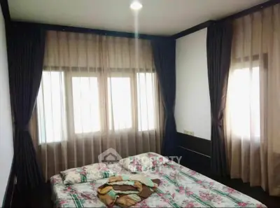 Cozy bedroom with floral bedding and large windows with elegant curtains.