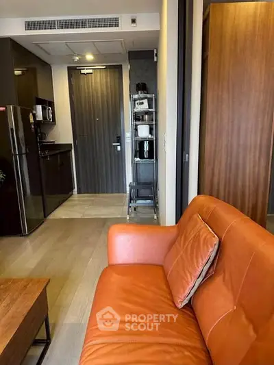 Modern apartment interior with leather sofa and compact kitchen area featuring sleek appliances.