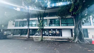 Modern building exterior with large windows and lush trees, ideal for commercial or residential use.