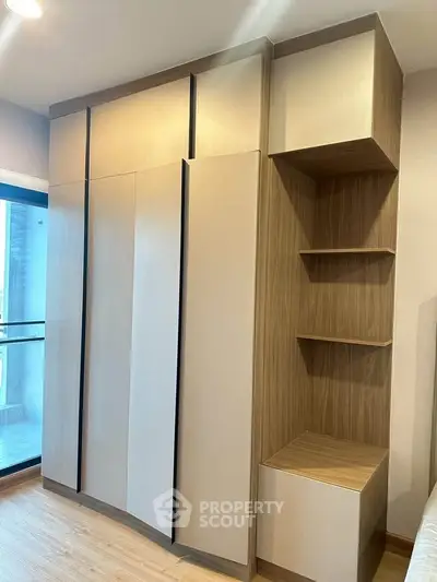 Modern bedroom with built-in wooden wardrobe and shelving, featuring sleek design and ample storage space.