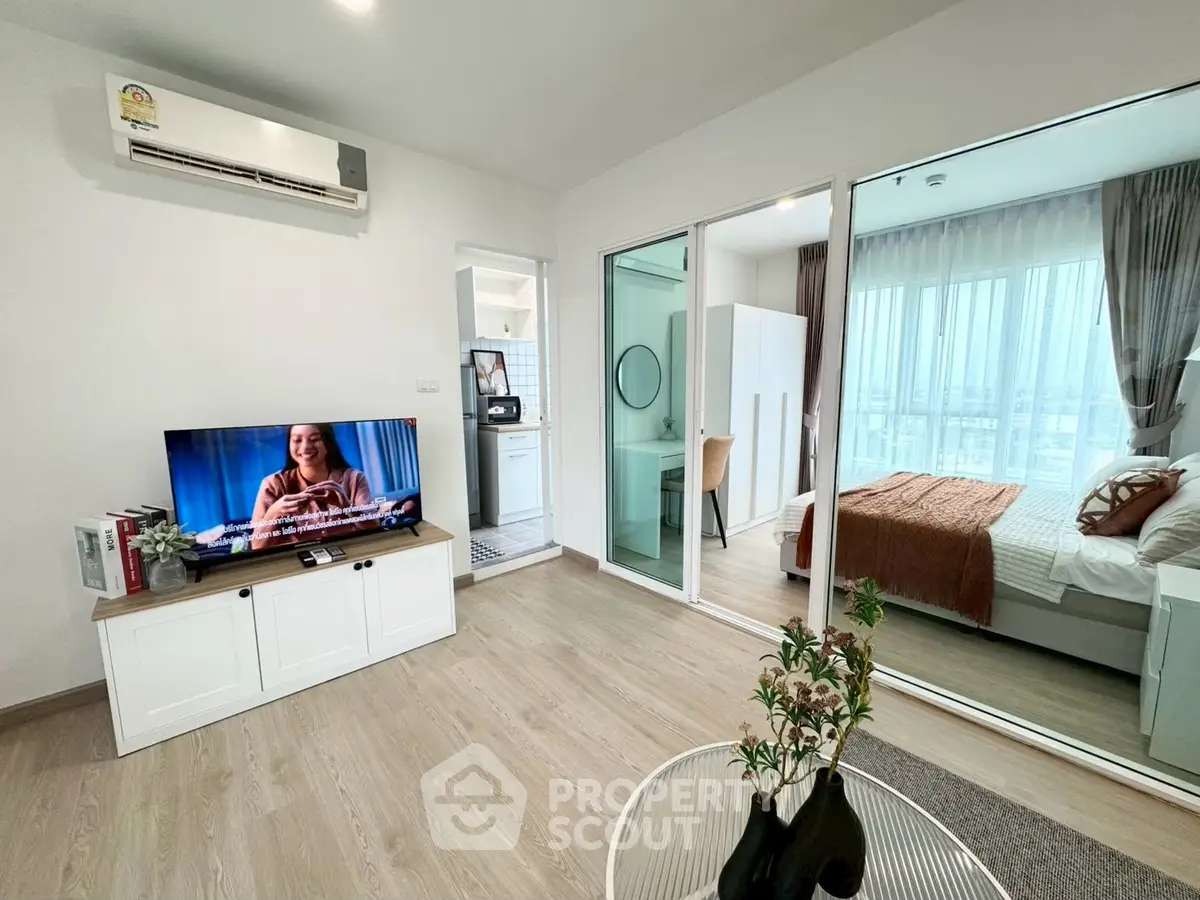 Modern living room with TV and view into cozy bedroom through glass doors.