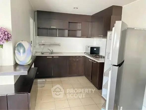 Modern kitchen with dark wood cabinets and stainless steel appliances in a cozy apartment.