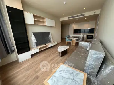 Modern living room with open kitchen, featuring sleek furniture and wooden flooring.
