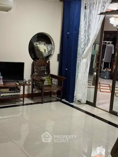 Elegant living room with polished floors, vintage chair, and modern TV setup, leading to a stylish wardrobe area.