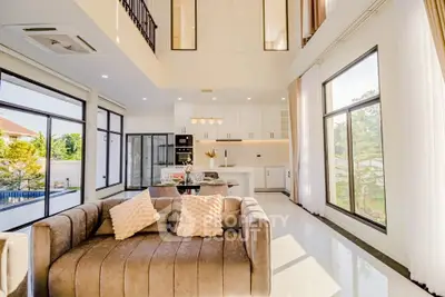 Luxurious open-plan living room with high ceilings and modern kitchen in a sunlit home.