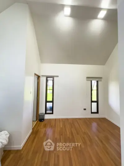 Spacious room with high ceiling and wooden flooring, perfect for modern living.