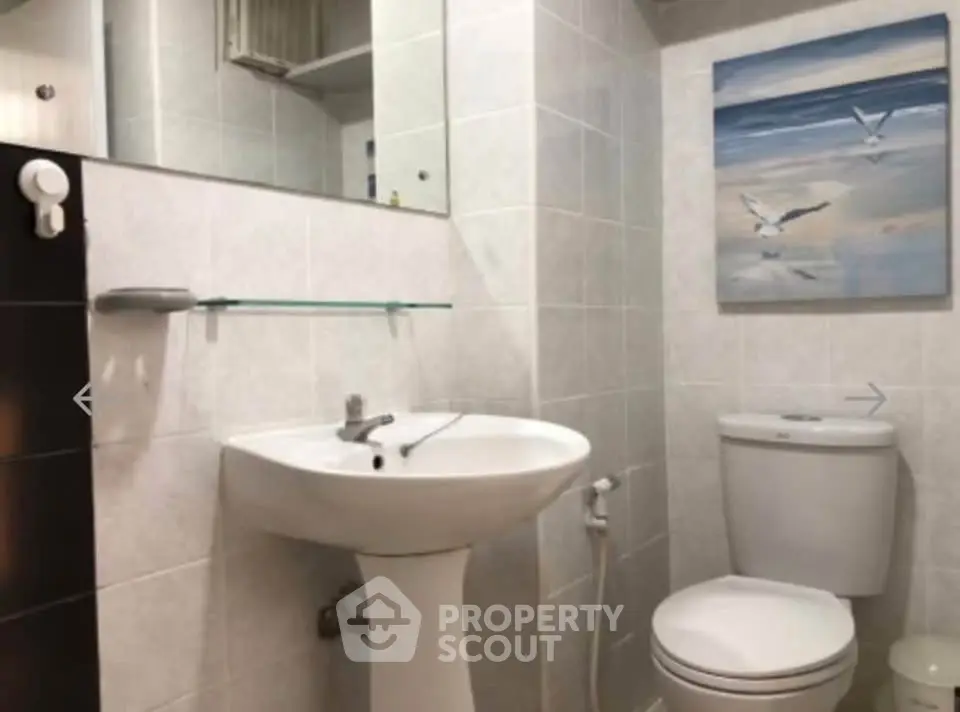 Modern bathroom with pedestal sink and wall art, featuring sleek white tiles and contemporary fixtures.