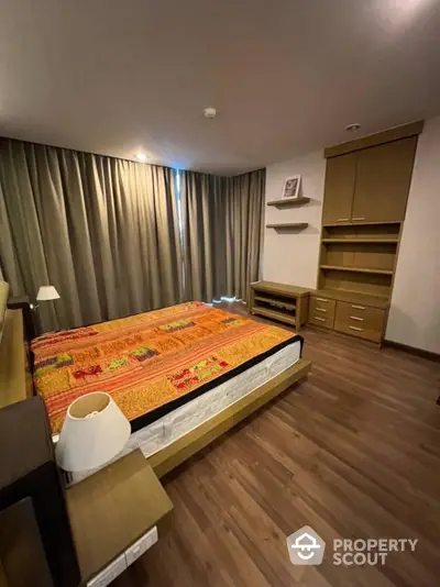 Cozy bedroom with warm wooden flooring, a large comfortable bed, elegant drapery, and ample storage space, perfect for restful nights and stylish living.