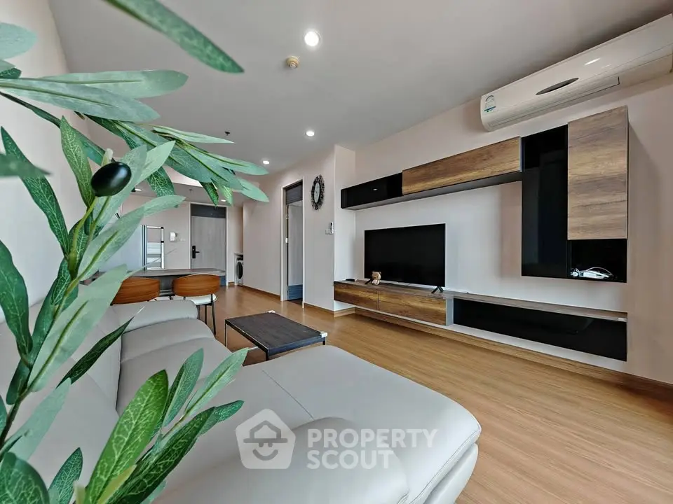 Modern living room with sleek furniture and wooden flooring, featuring a wall-mounted TV and air conditioning.