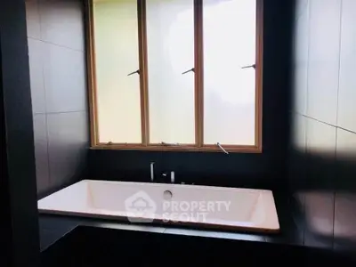 Modern bathroom with sleek black tiles and a large bathtub under a window.