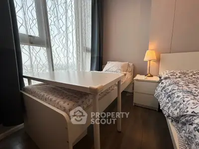 Cozy bedroom with twin beds, elegant lamp, and large window with sheer curtains.