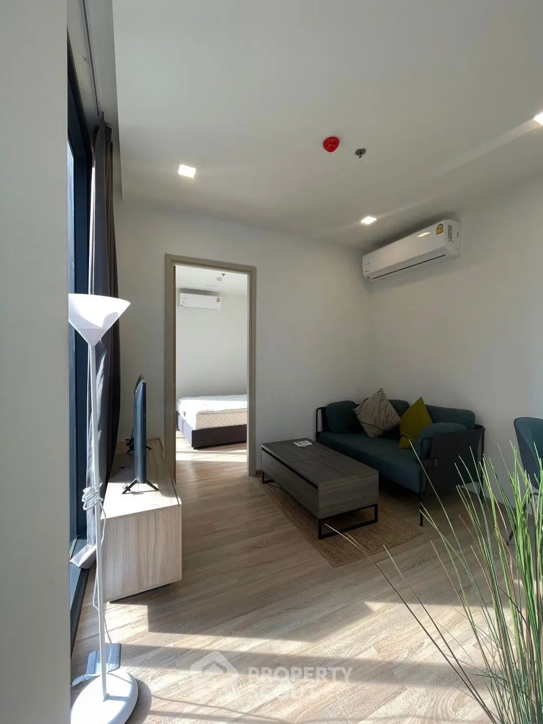 Modern living room with natural light and sleek furniture, leading to a cozy bedroom.