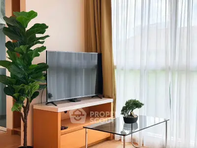 Modern living room with large TV, stylish furniture, and natural light from floor-to-ceiling windows.