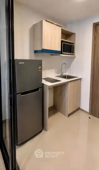 Modern compact kitchen with fridge, microwave, and sleek cabinetry in a stylish apartment.