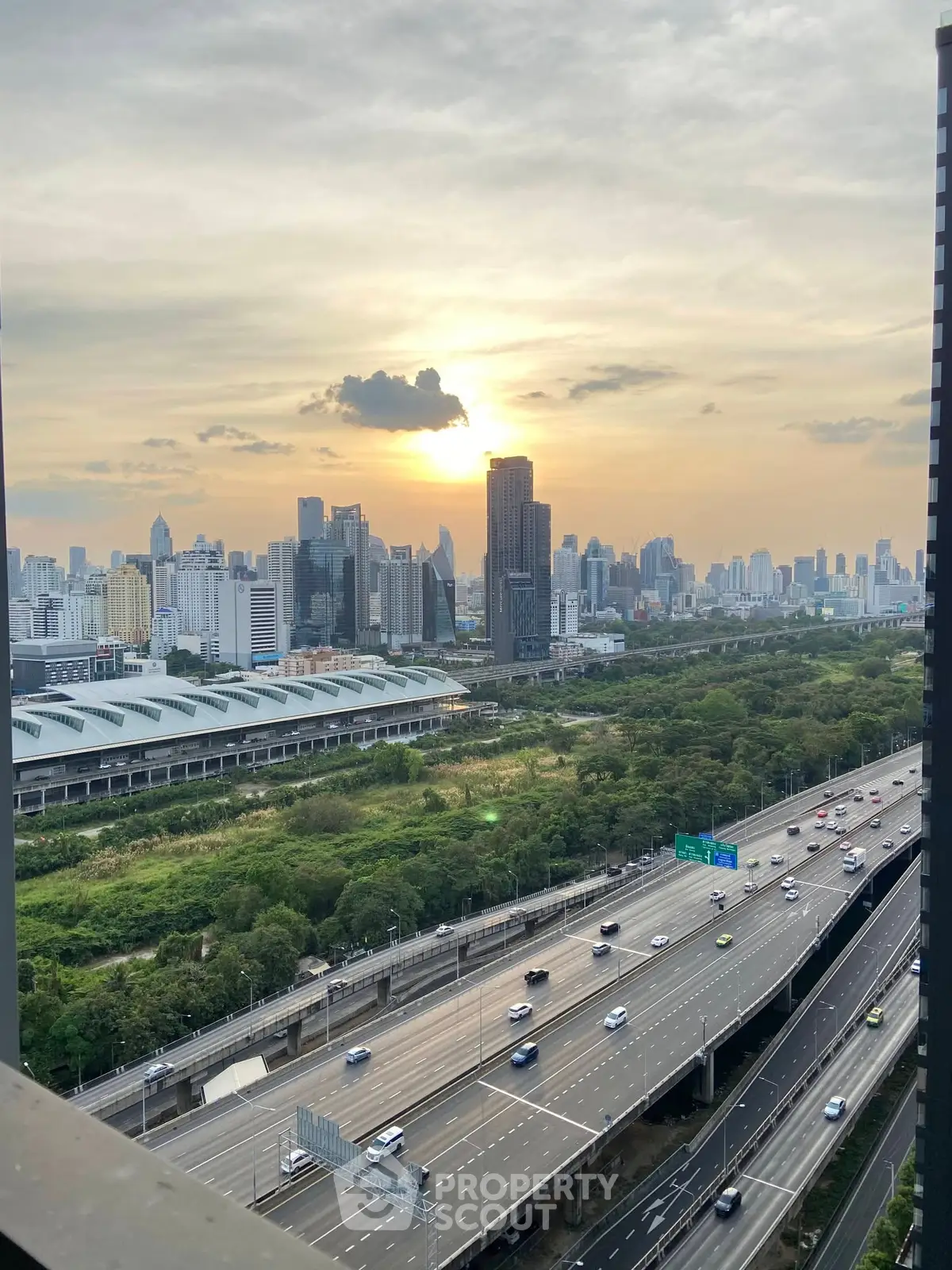 Stunning cityscape view from high-rise building at sunset, showcasing urban skyline and lush greenery.