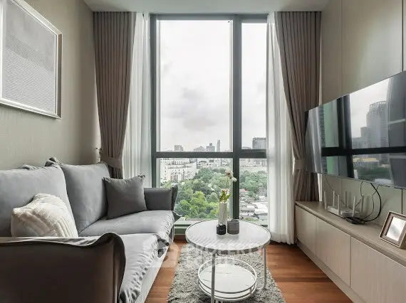 Modern living room with large window offering city view, cozy sofa, and sleek TV setup.
