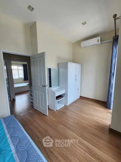 Spacious bedroom with wooden flooring and modern furniture in a bright apartment.