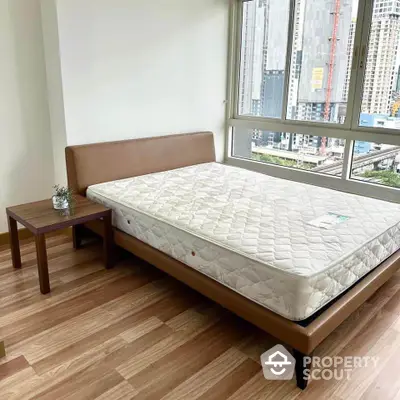 Modern bedroom with city view, featuring a stylish bed and wooden side table.