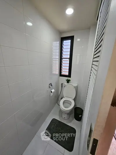 Compact modern bathroom with white tiles and natural light.