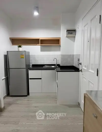 Modern compact kitchen with sleek design and stainless steel fridge in a cozy apartment.