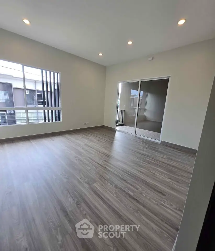 Spacious modern living room with large windows and balcony access, featuring elegant wood flooring.