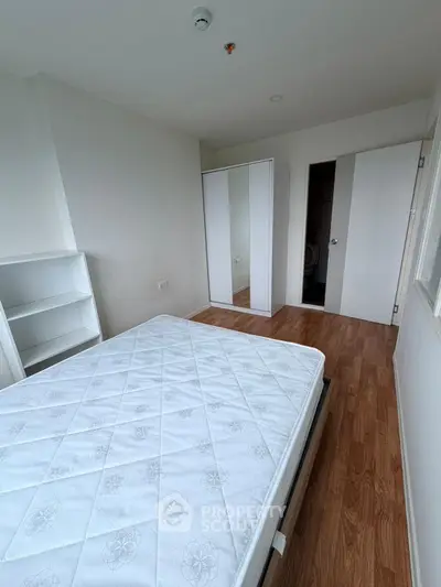 Spacious bedroom with wooden flooring and mirrored wardrobe in modern apartment.