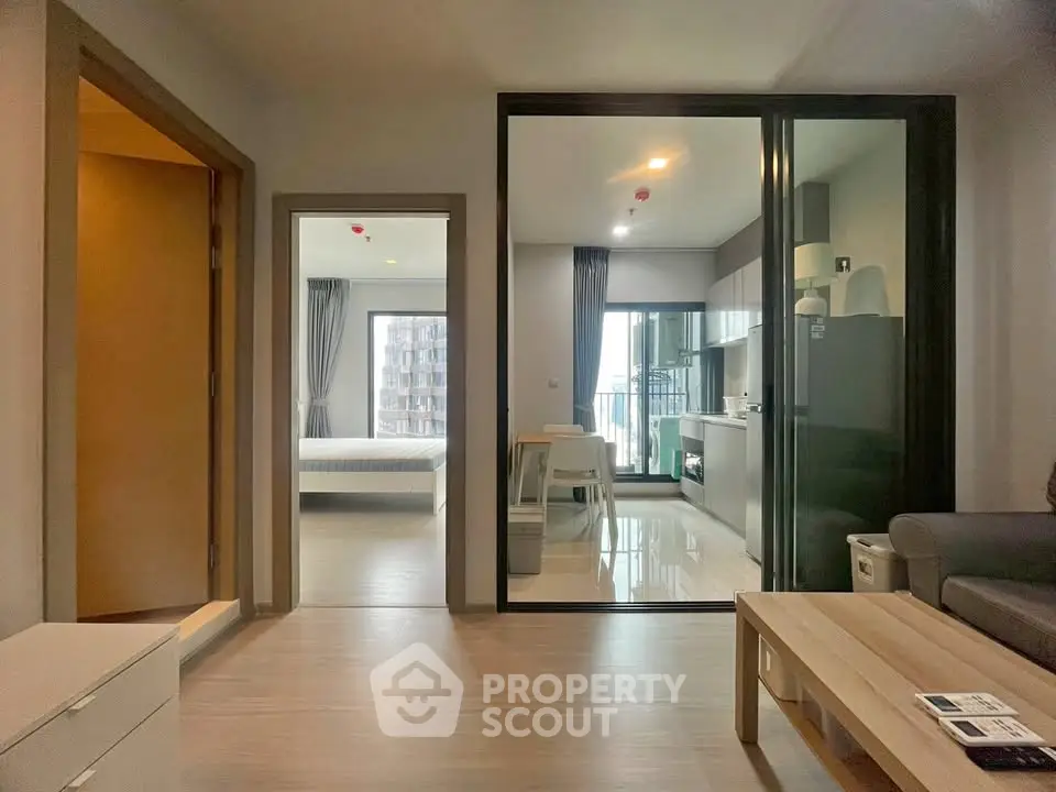 Modern apartment interior with open layout kitchen and cozy living area, featuring large windows for natural light.