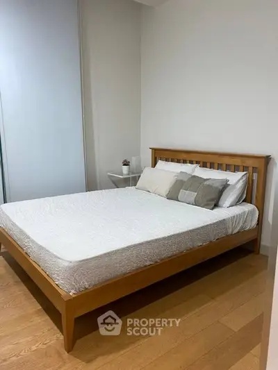 Cozy bedroom with wooden bed frame and minimalist decor, perfect for relaxation.