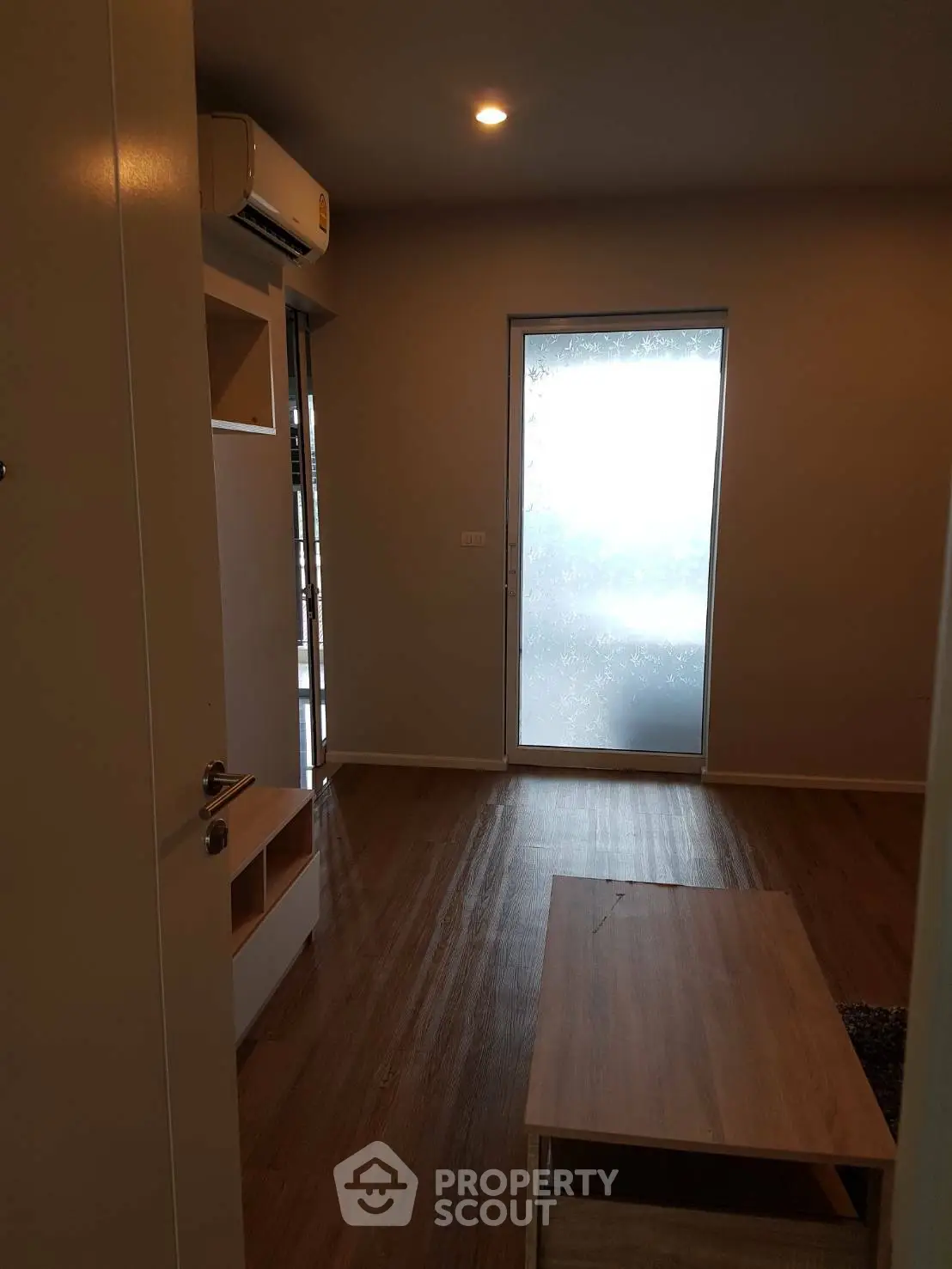 Cozy living room with wooden flooring and frosted glass door, featuring modern air conditioning.