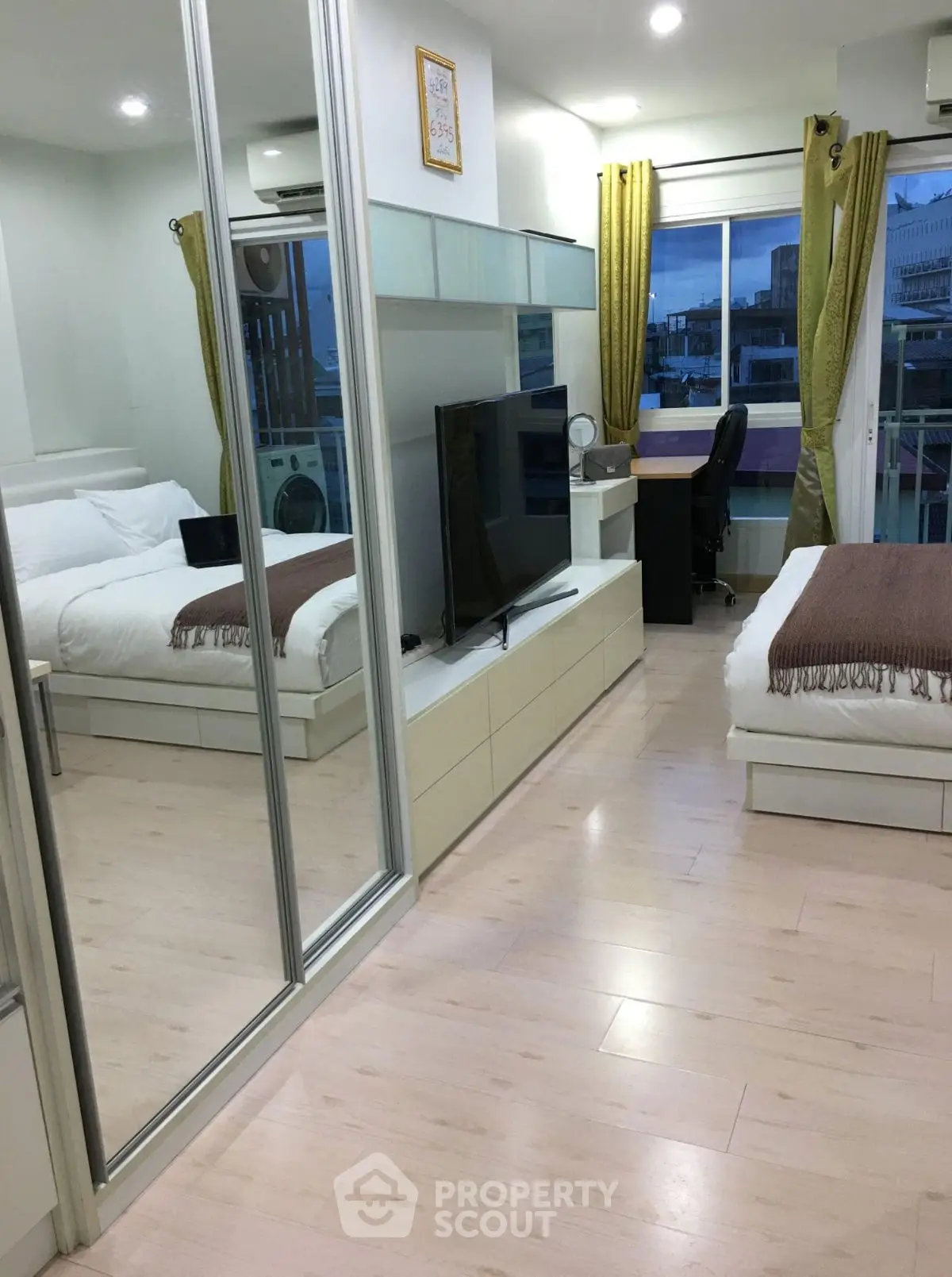 Modern bedroom with mirrored closet and city view, featuring sleek furniture and cozy ambiance.