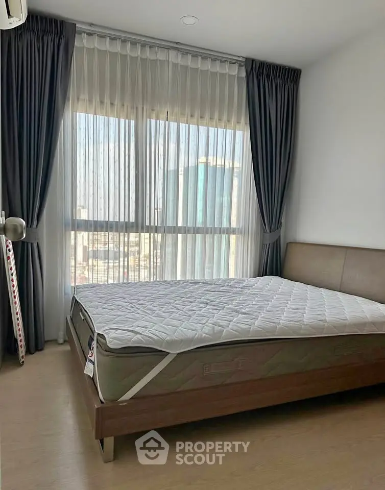 Modern bedroom with large window and city view, featuring a comfortable bed and elegant curtains.