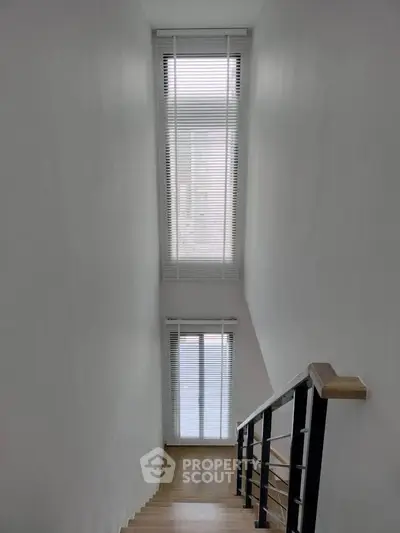 Modern staircase with tall windows and sleek railing in a minimalist home interior.