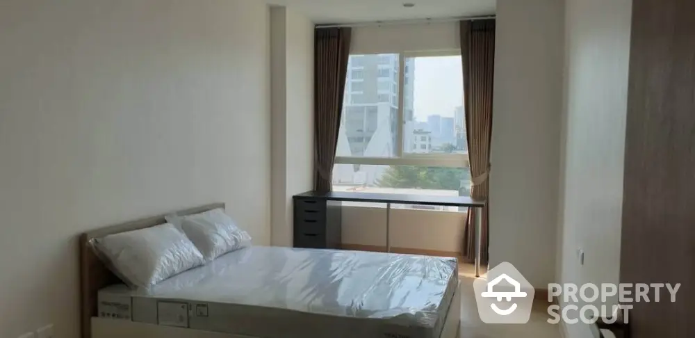 Modern bedroom with large window and city view, featuring a comfortable bed and sleek desk.