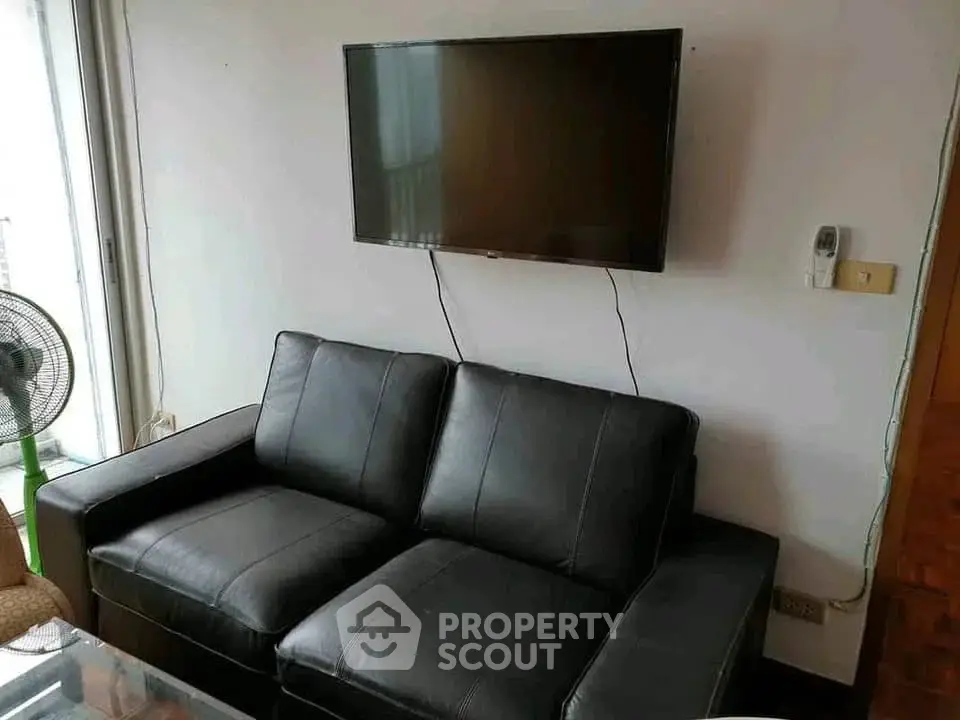 Modern living room with sleek black leather sofa and wall-mounted TV, perfect for relaxation.