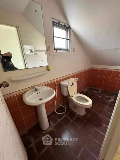 Cozy attic bathroom with sloped ceiling, featuring a pedestal sink and toilet, ideal for compact spaces.