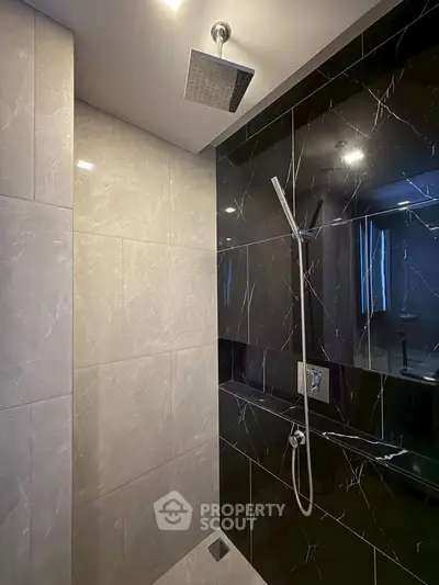 Luxurious modern bathroom with sleek black and white marble tiles and rainfall showerhead.