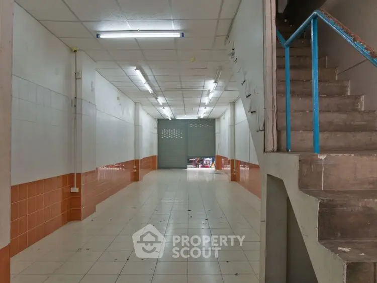 Spacious commercial space with tiled flooring and staircase, ideal for retail or storage.