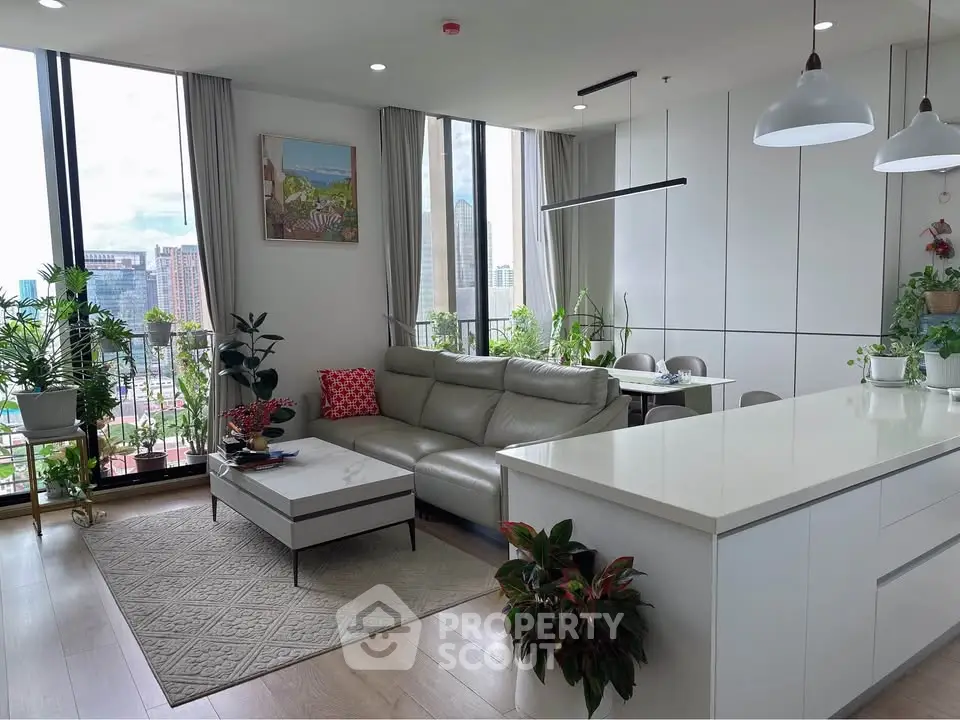 Modern living room with open kitchen, large windows, and city view, featuring stylish decor and abundant natural light.