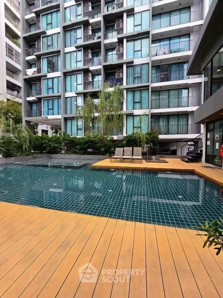Modern apartment building with poolside deck and lush greenery.