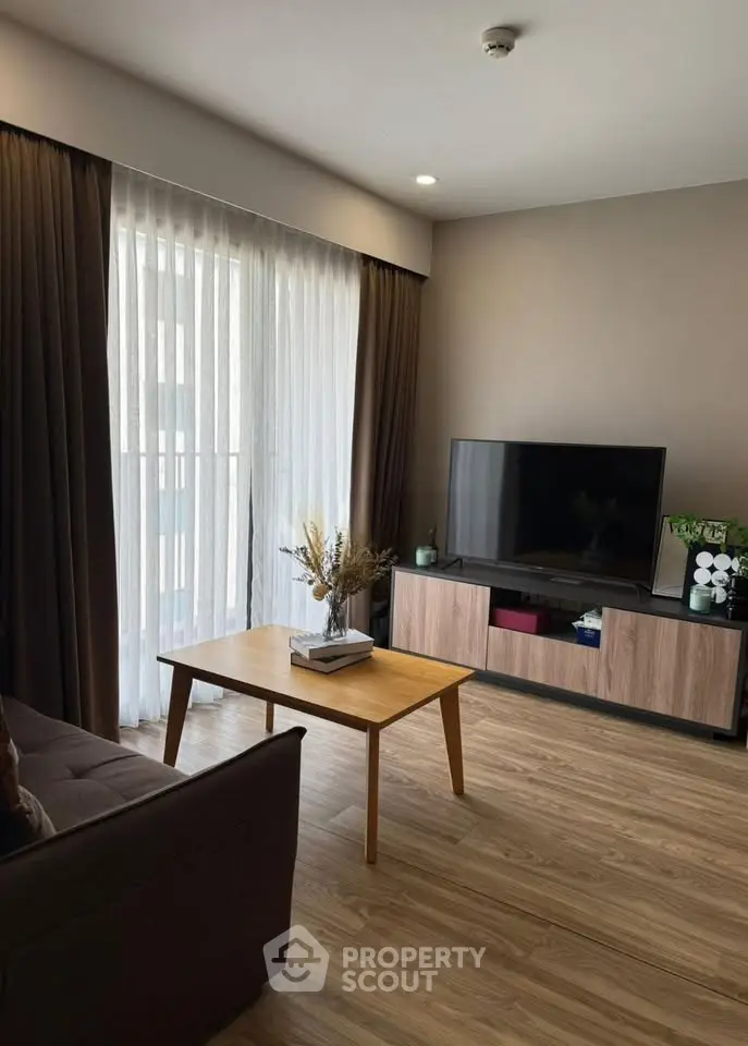 Modern living room with sleek wooden flooring, large TV, and elegant curtains for a cozy ambiance.