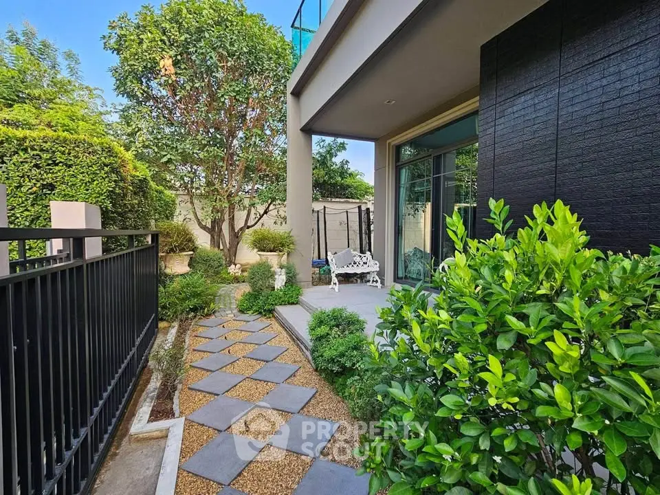 Charming garden path leading to a modern home's entrance with lush greenery and elegant outdoor seating.