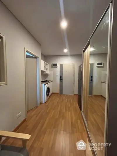 Modern apartment hallway with wooden flooring and mirrored wardrobe