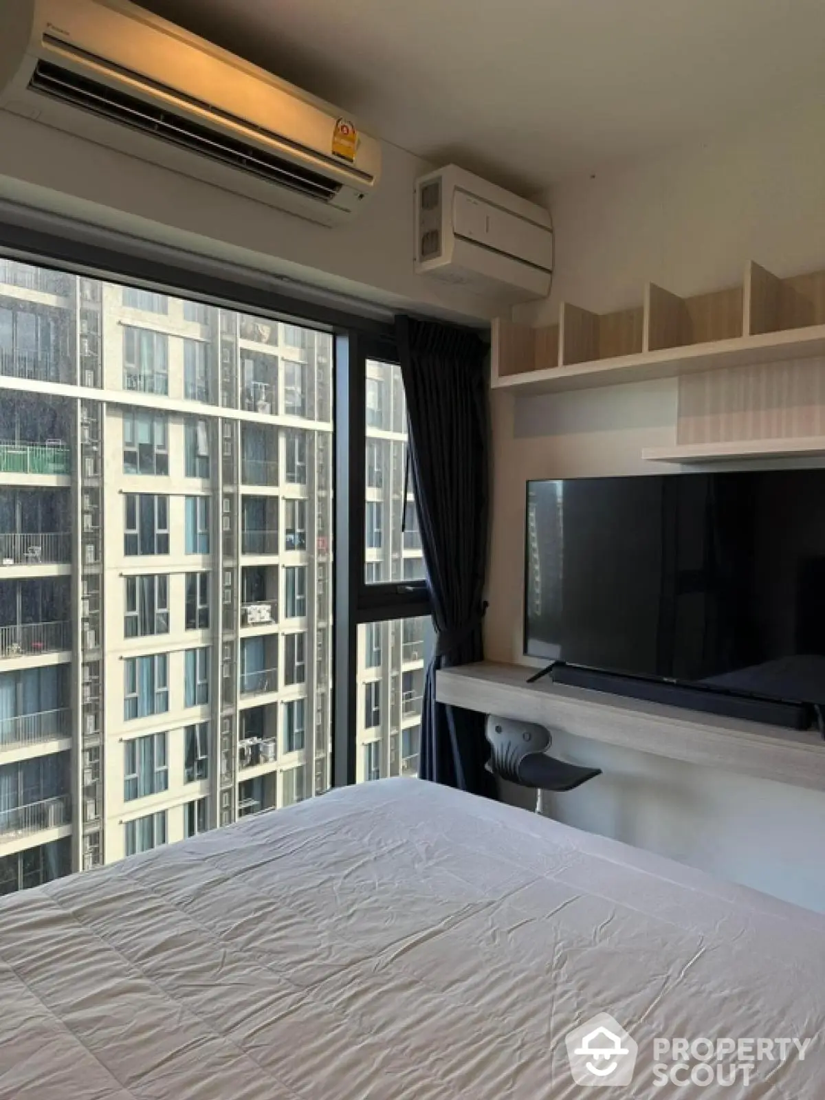 Modern bedroom with large window and city view, featuring air conditioning and wall-mounted TV.