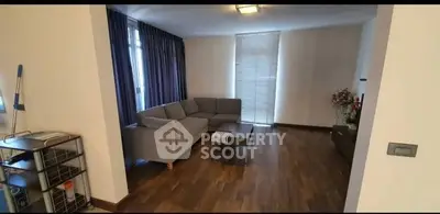 Spacious living room with modern decor and wooden flooring, featuring a cozy gray sofa and natural light.