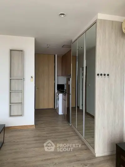 Modern apartment interior with mirrored closet and wooden flooring, featuring a compact kitchen area.