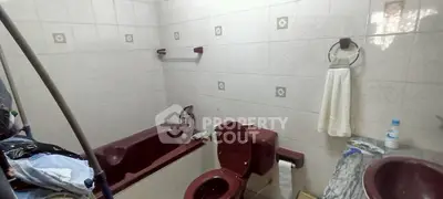 Spacious bathroom with maroon fixtures and tiled walls, featuring a bathtub and ample storage space.